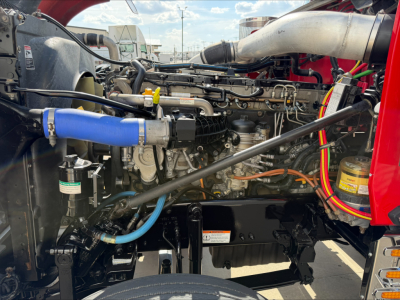 Tractor cab-less engine bay of a Western Star 4900 showing large blue radiator hose, silver exhaust, various hoses, wiring, and a yellow filter, engine components visible.