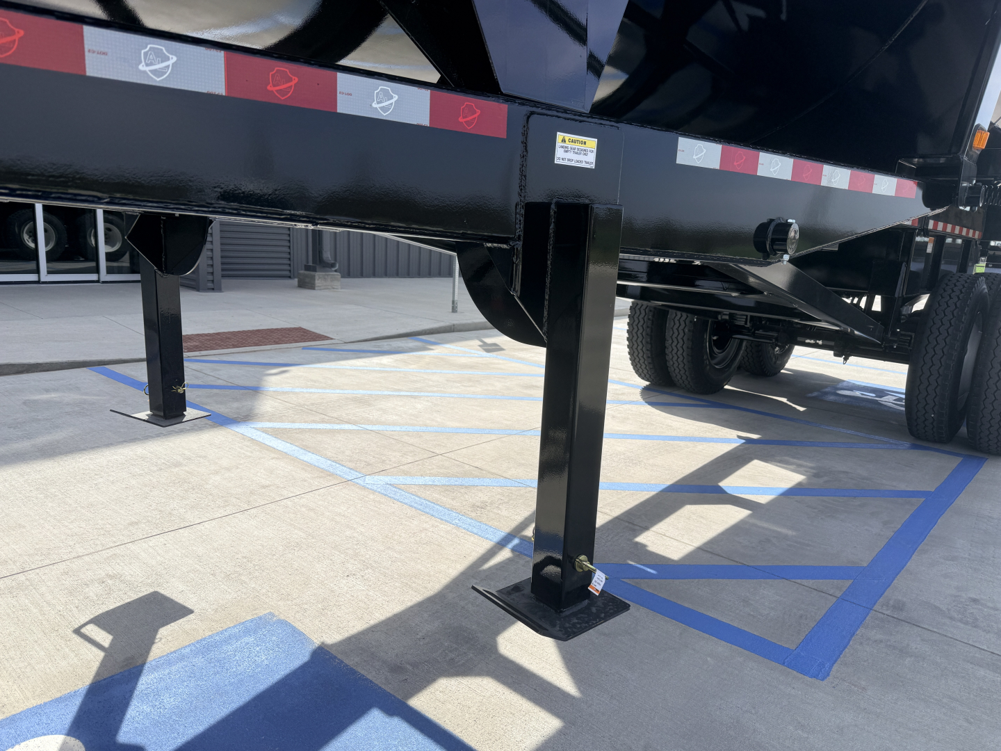 Trailer leg of Armor Lite SHD 28/48 dump trailer showing adjustable support leg with base plate and wheel in background.