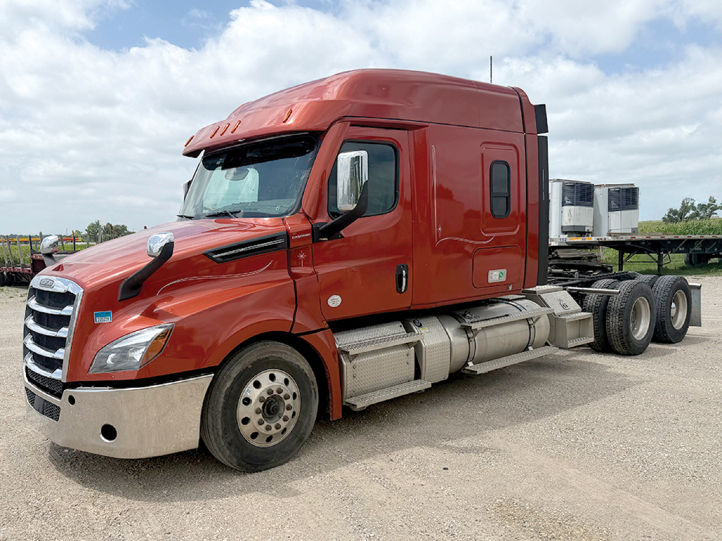 Red Freightliner Cascadia126 tractor cab side view showing exterior fuel tanks and dual rear axles.