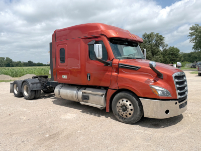 Red Freightliner Cascadia126 cab truck in a gravel lot, side view showing fuel tanks, front bumper, and wheels.
