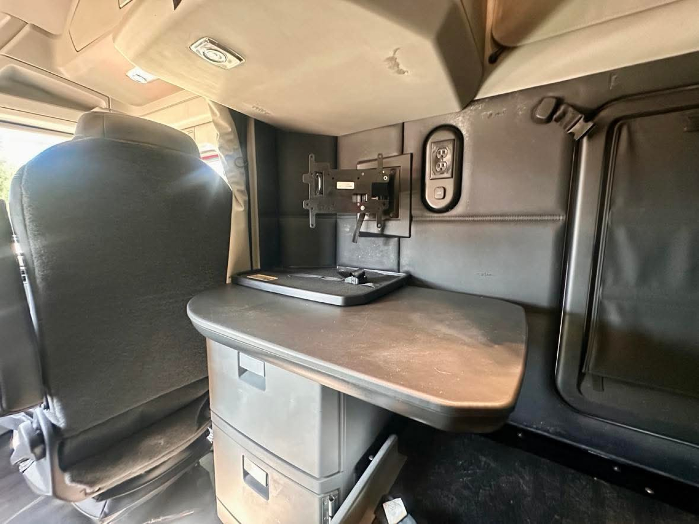 Kenworth T680 cab interior showing flip-down table with storage drawers and mount for monitor, side panel with power outlet and overhead shelf.