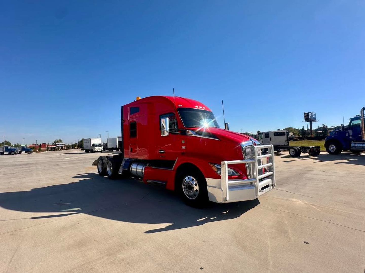 Kenworth T680 conventional sleeper semi-truck in red, front-left three-quarter view, chrome bumper and exhaust, parking lot background.