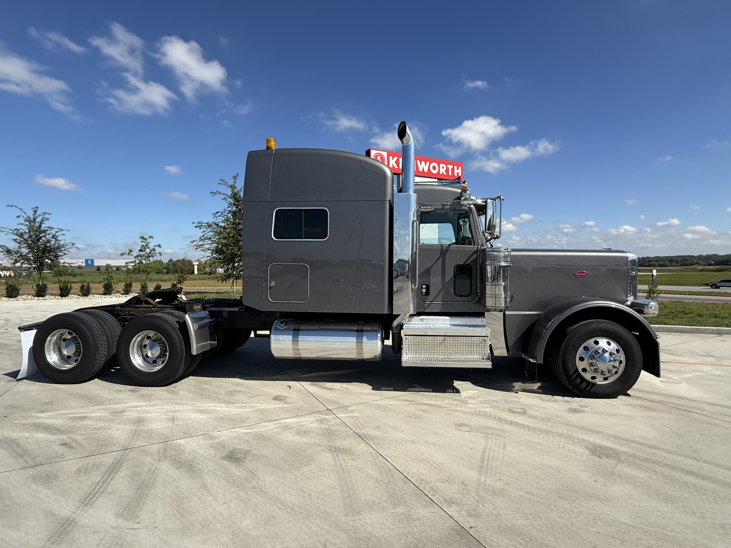 Peterbilt 389 conventional sleeper truck side view showing grey cab, dual rear axles, fuel tanks, and chassis with long wheelbase.