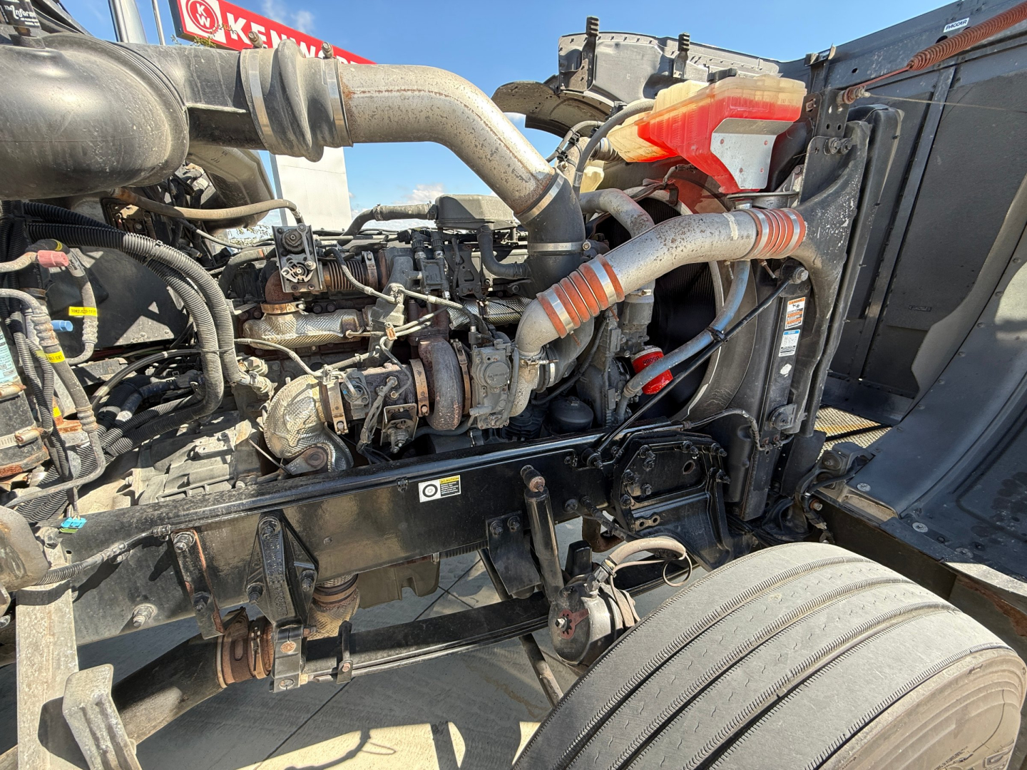 Peterbilt 389 engine bay showing air intake hoses, coolant hoses, and engine components. Visible text includes VIN and stock numbers in listing context; however no legible labels or fluid specifications visible in image.