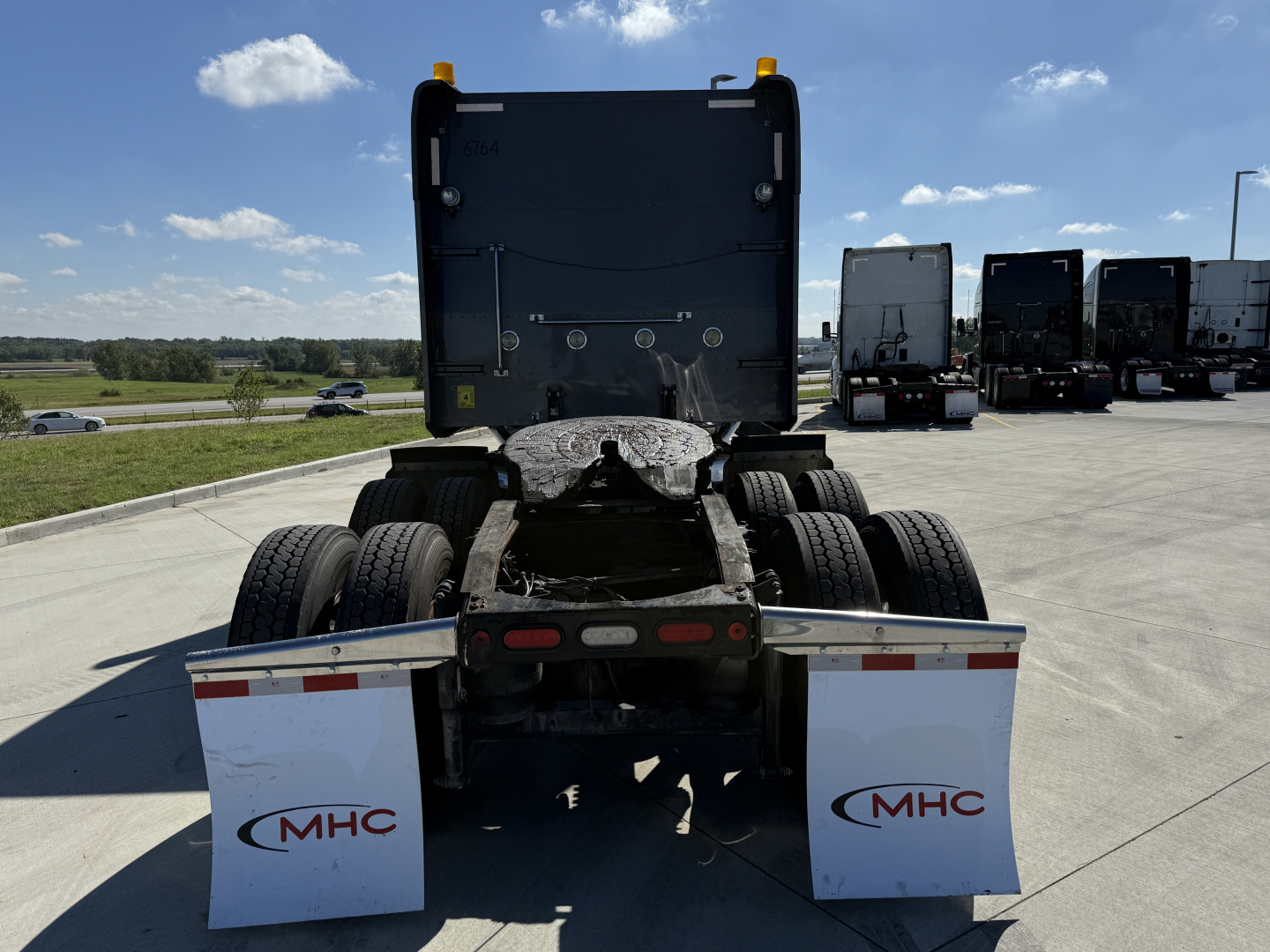 Peterbilt 389 sleeper tractor rear view showing dual rear axles, trailer-free fifth wheel, mud flaps with MHC logo, daytime sky.