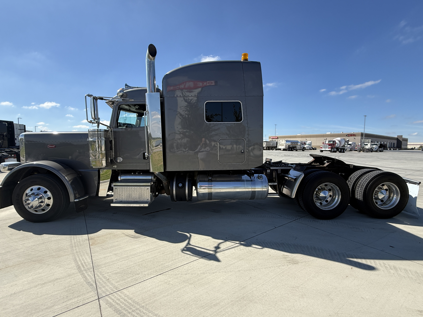 Peterbilt 389 sleeper cab tractor in side profile showing single cab, chrome exhaust stack, dual rear axles, fuel tanks, and gray paint.