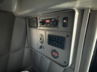 Peterbilt 389 cab interior panel showing controls: Berrik or Berl? knob cluster, two circular knobs, 12V DC outlet, air vent, and a round gauge. Visible text includes power switch markings and indicator lights.