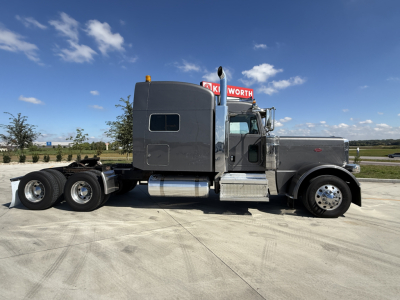 Peterbilt 389 conventional sleeper truck side view showing grey cab, dual rear axles, fuel tanks, and chassis with long wheelbase.