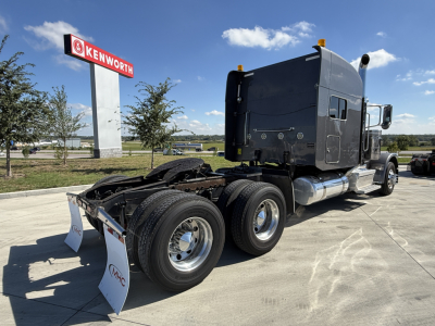 Peterbilt 389 tractor truck rear view showing dual rear axles and sleeper cab, in-service condition with Kenworth lot in background.