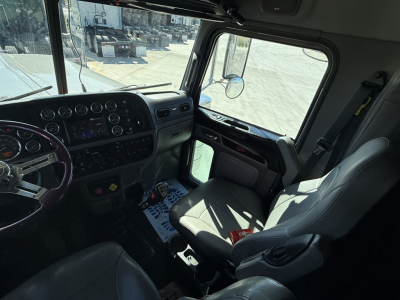 Peterbilt 389 cab interior showing steering wheel, dashboard gauges, and driver's seat with window view.