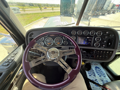 Peterbilt 389 interior dashboard and purple steering wheel in-cab view, with gauges and infotainment display visible.