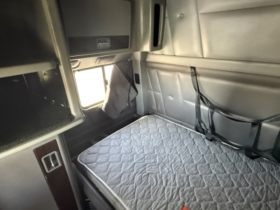 Peterbilt 389 sleeper cab interior showing bed with quilted mattress, storage compartments, and side panels with wiring harnesses.