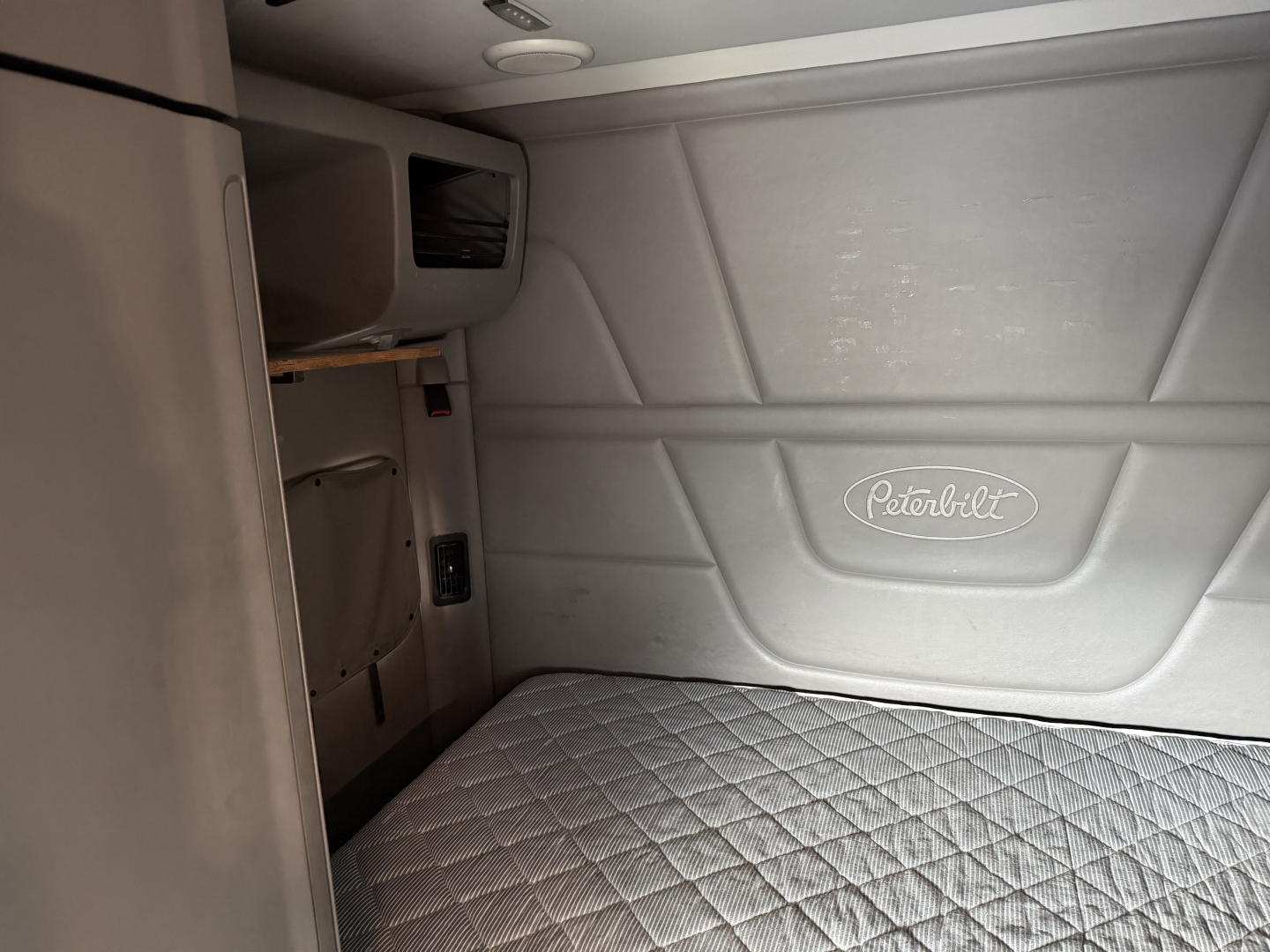 Peterbilt truck cab interior side wall with Peterbilt emblem and quilted sleeper bed surface visible.