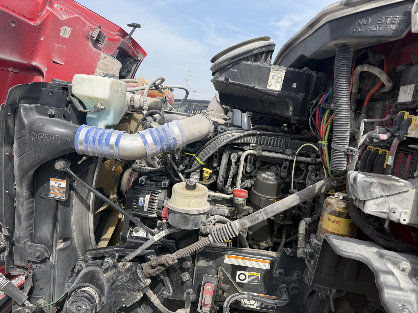 Partially visible diesel engine bay of a 2017 Peterbilt 579 with various hoses, reservoirs, and wiring harnesses.