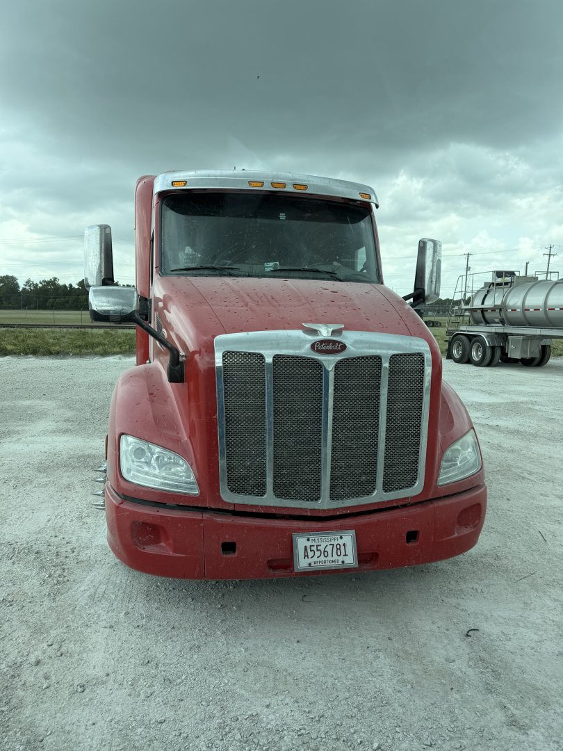 Peterbilt 579 truck front view in red paint with large chrome grille, headlights, side mirrors, and license plate A556781; VIN plate not visible.