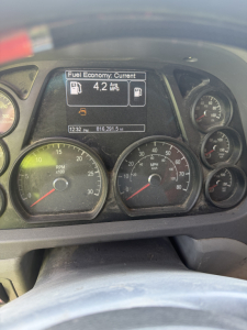 Peterbilt dashboard showing fuel economy display: 'Fuel Economy: Current 4.2 Avg MPG' with multiple gauges including RPM, speed, and other indicators.