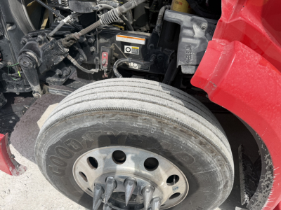 Peterbilt 579 engine bay with front dual tires and wheel, visible hoses, and warning labels.