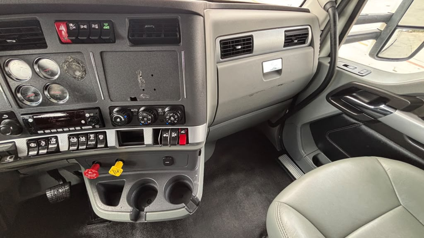 Kenworth T680 cab interior dash and steering area with gauges, controls, and cup holders visible.