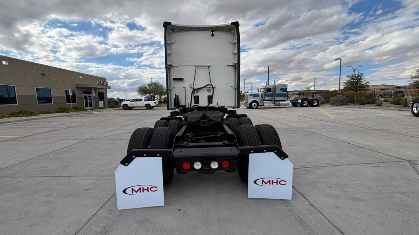 Kenworth T680 chassis view showing rear cab, white mud flaps with MHC logo and rear area with tires.