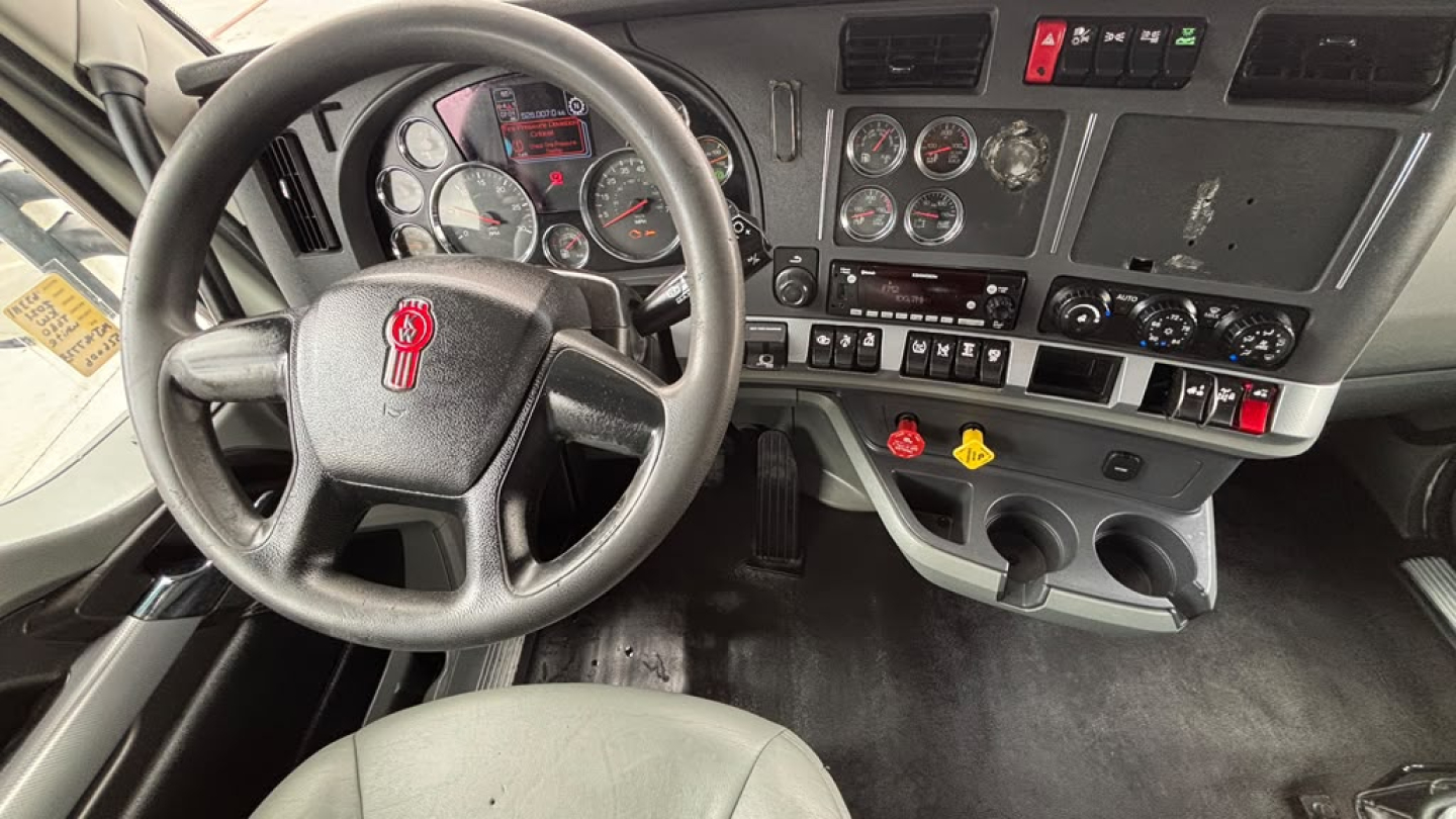 Kenworth T680 cab interior showing steering wheel, dashboard gauges, and control panel with switches and knobs.