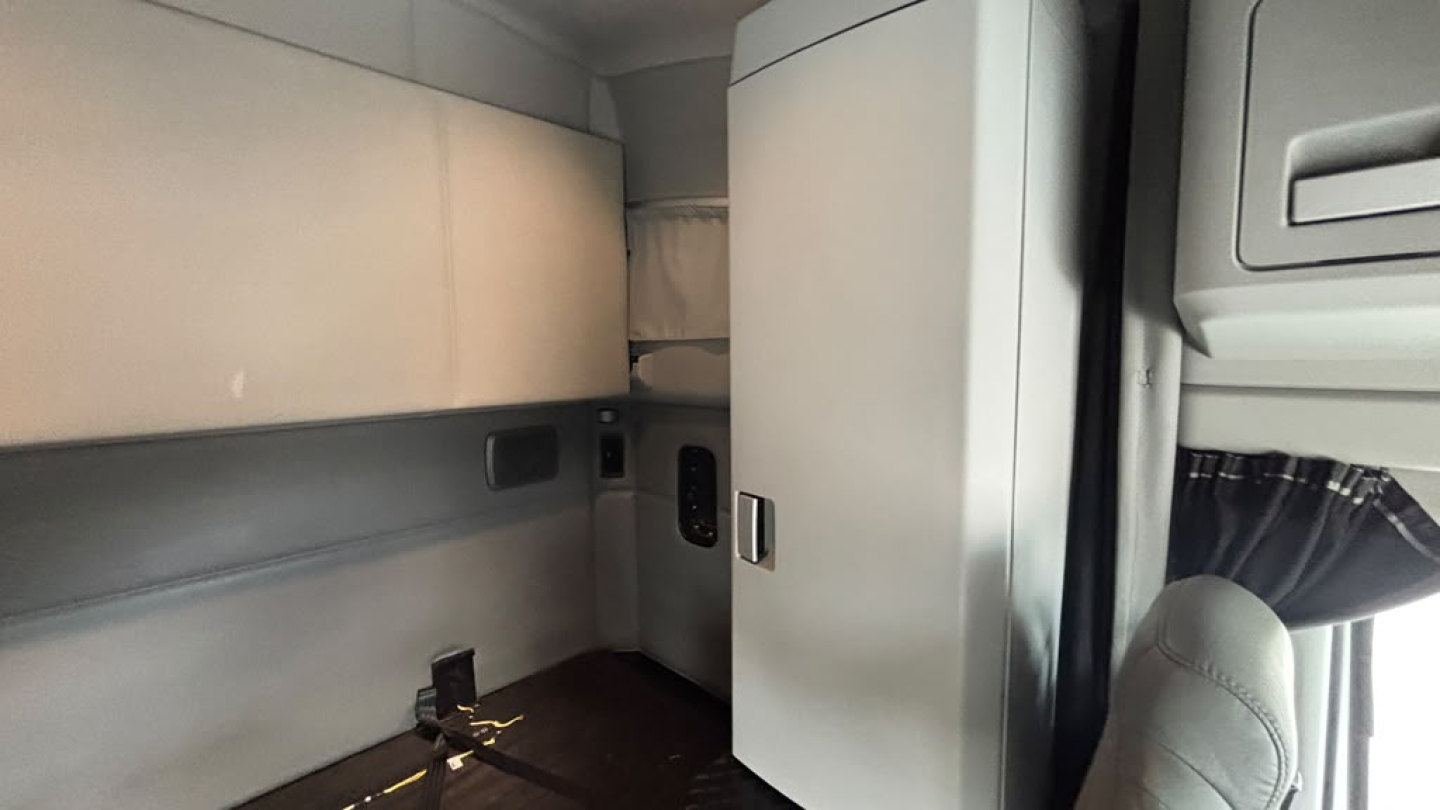 Kenworth T680 cab interior showing sleeper area and storage cabinets with soft gray upholstery.