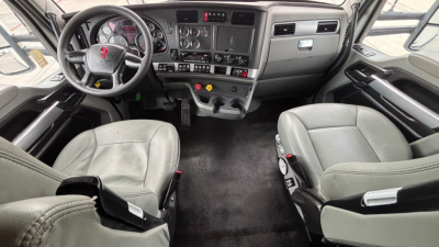 Kenworth T680 cab interior showing steering wheel, dashboard with gauges, center console, two seats, and floor mats.
