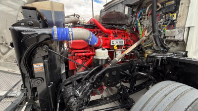 Kenworth T680 engine bay showing red diesel engine with blue silicone hose, black radiator, and wiring harnesses in engine compartment.