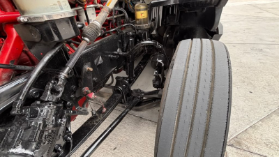Kenworth T680 front suspension and drive components showing frame rails and a front tire with visible hydraulic lines and wiring