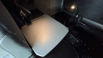 Interior of a Kenworth truck cab with a fold-out bunk table and dark control panels visible.