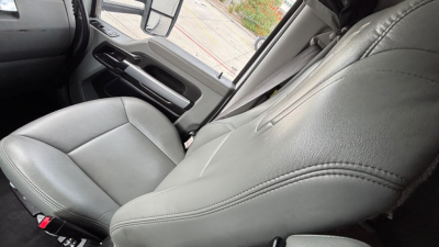Truck cab interior showing front passenger seat and door panel from a Kenworth T680, gray leather seats, light gray upholstery, steering wheel partially visible.