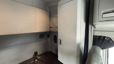 Kenworth T680 cab interior showing sleeper area and storage cabinets with soft gray upholstery.