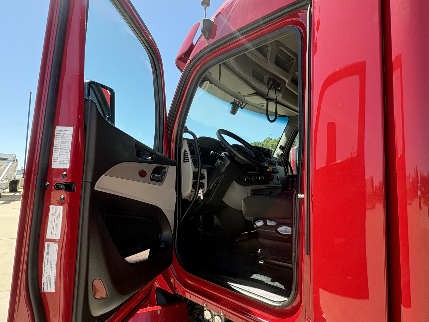 Truck cab interior view of a red Peterbilt 579 from the open driver's door showing the steering wheel, dash, and seating.