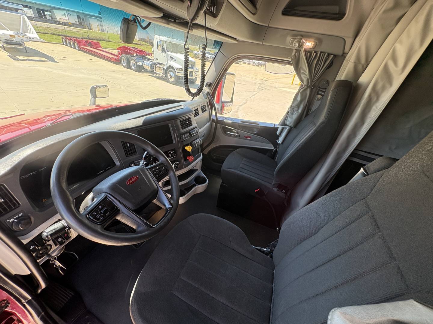 Peterbilt 579 truck cab interior dashboard and steering wheel view showing driver seat and passenger seat, with overhead sun visor and center console.