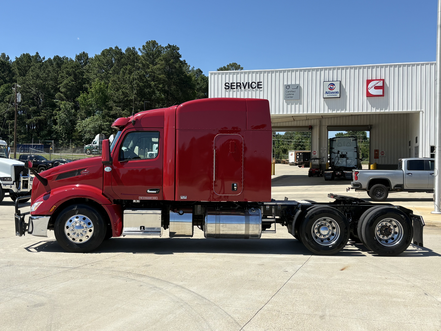 Peterbilt 579 tractor-trailer cab in red, side view, with chrome fuel tanks and dual rear axles, parked in front of service building.