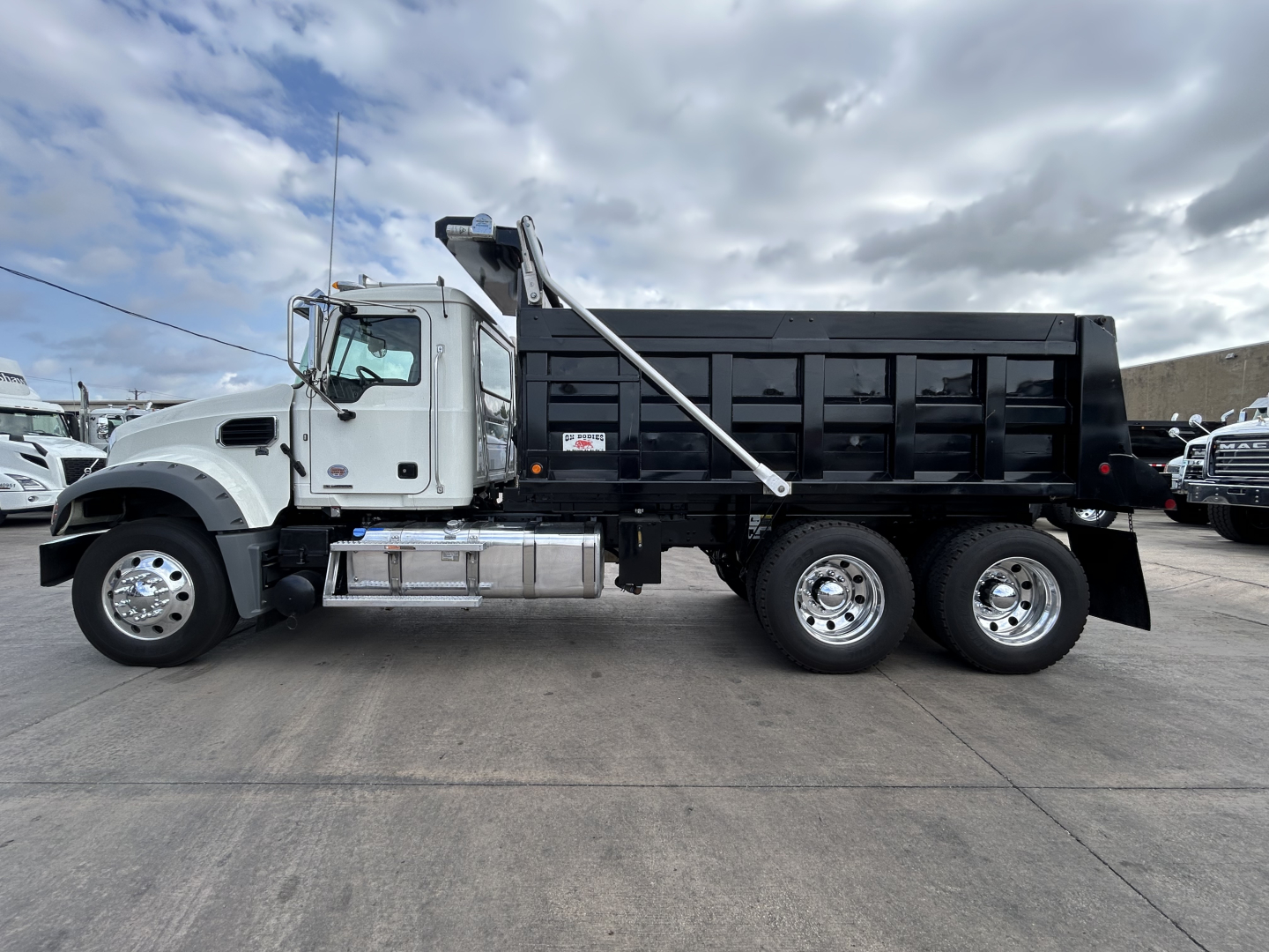 Mack GR64F dump truck in-profile showing black dump bed, white cab, chrome fuel tanks, and dual rear axles.