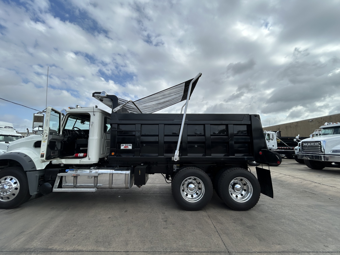 Mack GR64F dump truck with open dump bed and raised tailgate, side view showing dual rear axles and chrome wheels.