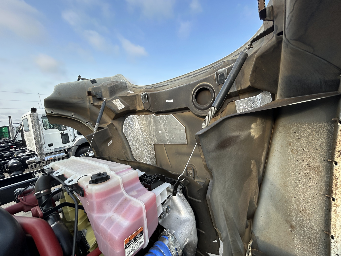 Truck engine bay showing coolant reservoir and mounting area of a 2025 Mack GR64F dump truck in-service with pink coolant reservoir and surrounding framework.