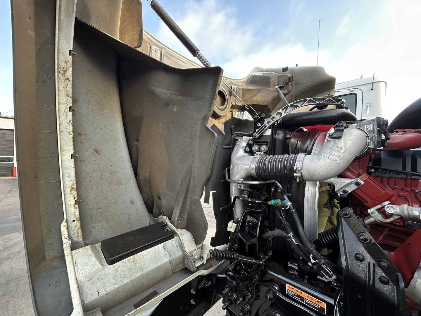 Mack GR64F engine bay showing air intake, turbocharger piping, and hydraulic components in a dump truck.