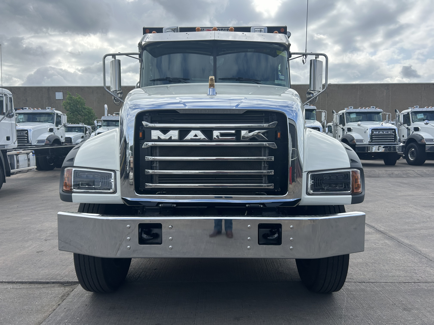 Truck front view of a white Mack GR64F dump truck showing large chrome grille with MACK logo, rectangular headlights, chrome bumper, day cab, side mirrors.