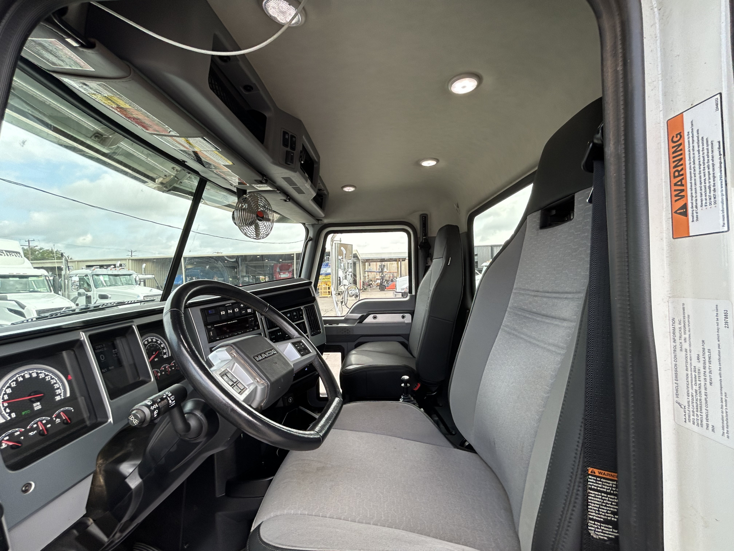 Interior of a 2025 Mack GR64F cab showing steering wheel, dashboard, and gray fabric seats.