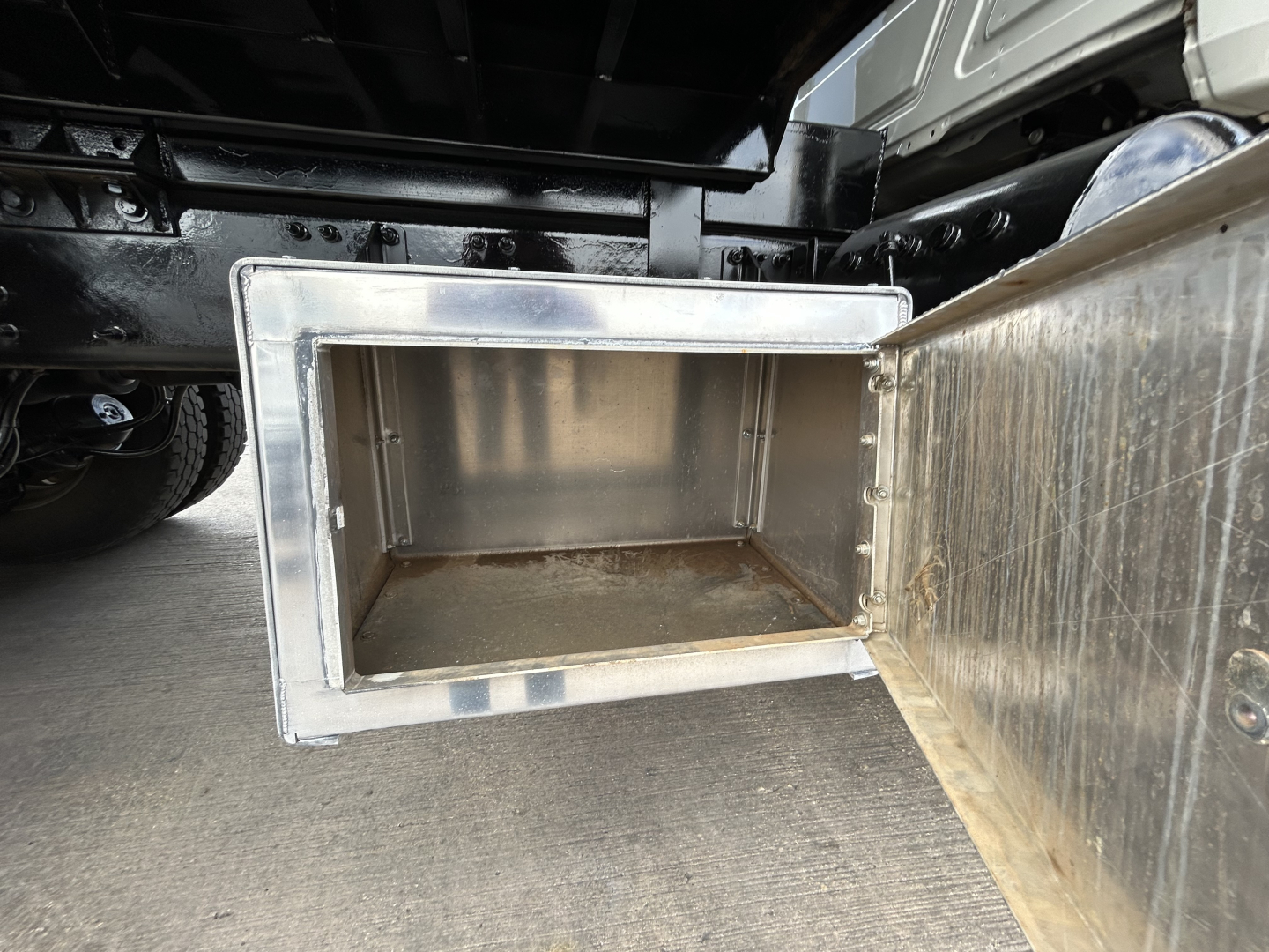 Dump truck undercarriage showing underbody storage box with open metal lid and empty interior.