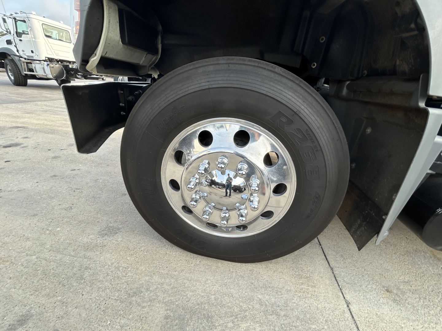 Mack GR64F wheel and front tire assembly showing polished chrome lug nuts and hub, part of a dump truck undercarriage.