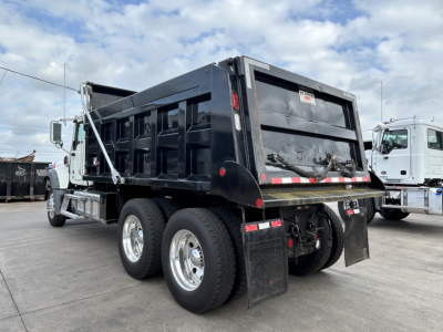 Dump truck rear and side view showing heavy-duty 6x4 chassis, black dump bed, dual rear axles, mud flaps, and chrome wheels on a Mack GR64F.
