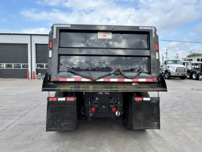 Dump truck bed of a 2025 Mack GR64F showing rear view with bumper and taillights, and mud flaps.