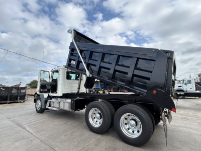 Mack GR64F dump truck in a raised bed with dual rear axles and silver wheels, side view showing hydraulic dump mechanism.