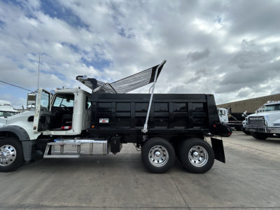 Mack GR64F dump truck with open dump bed and raised tailgate, side view showing dual rear axles and chrome wheels.