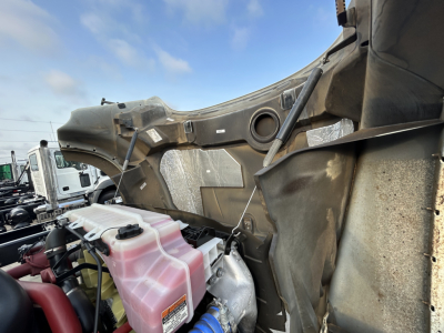 Truck engine bay showing coolant reservoir and mounting area of a 2025 Mack GR64F dump truck in-service with pink coolant reservoir and surrounding framework.