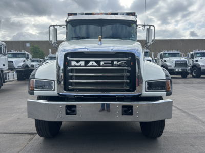 Truck front view of a white Mack GR64F dump truck showing large chrome grille with MACK logo, rectangular headlights, chrome bumper, day cab, side mirrors.