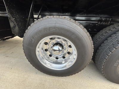 Wheel and tire of a Mack GR64F truck showing Bridgestone tire on polished chrome rim with lug nuts and black undercarriage.