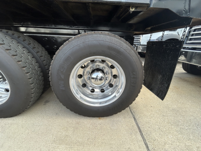 Truck wheel and tire on a Mack GR64F dump truck showing chrome wheel with lug nuts and black chassis, partial spare tire visible.